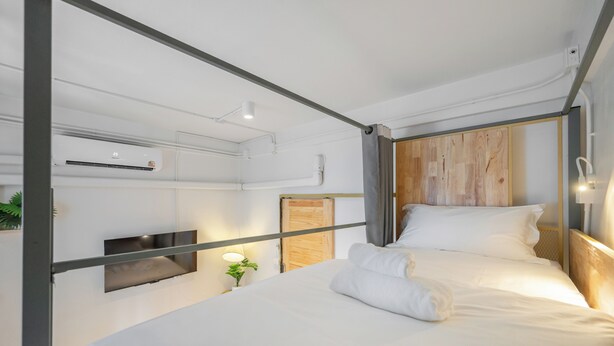 Una habitación de hotel moderna con cama, televisor de pantalla plana, aire acondicionado y una pequeña mesita de noche con lámpara y planta.