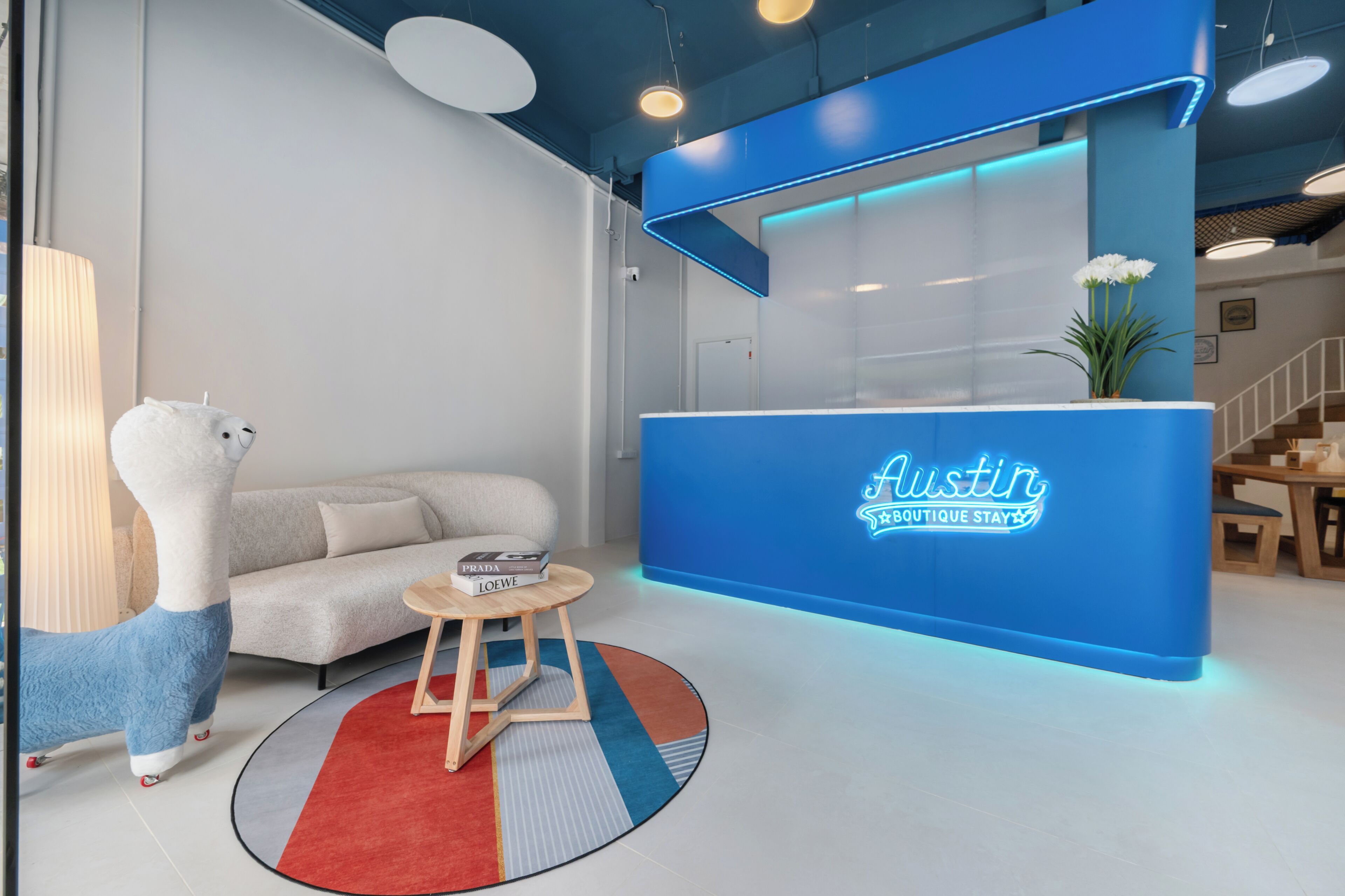 A modern reception desk with a blue accent, a plush sofa, a small wooden table with books, and a decorative lamp.