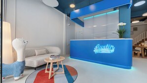 Un moderno mostrador de recepción con detalles azules, un sofá mullido, una mesita de madera con libros y una lámpara decorativa.
