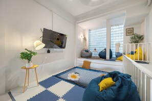 A modern living room with a blue and white patterned rug, a bean bag chair, a small table with a plant, and a television mounted on the wall. - Austin Boutique Stay Pratunam (Bangkok)