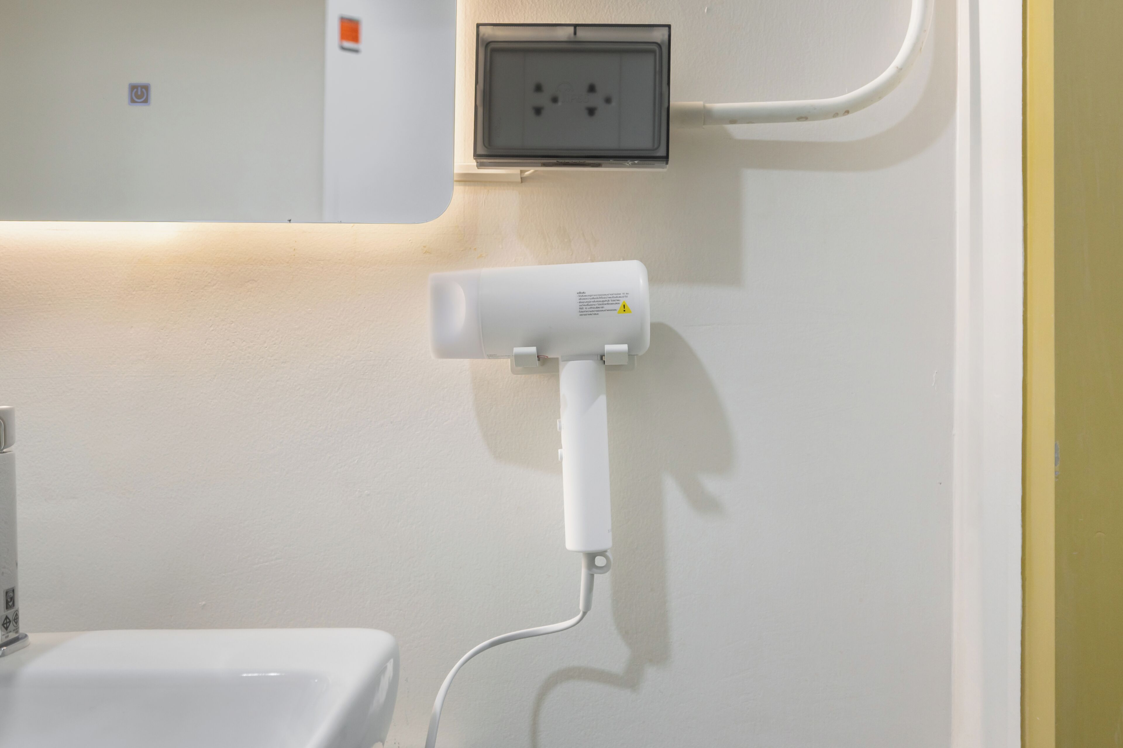 A bathroom with a white sink, a mirror, and a hairdryer mounted on the wall.