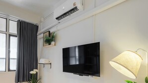 Una sala de estar moderna con un televisor de pantalla plana, aire acondicionado instalado en la pared, una lámpara y una planta en maceta.