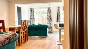 A spacious living area with a teal sofa, wooden flooring, and a dining area with a table and chairs. - Tranquil Turquoise - 3 Bed House With Parking (Bracknell)