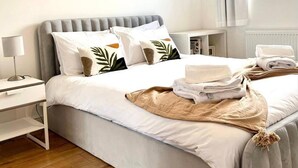 A neatly made bed with white bedding, a grey headboard, and a bedside table with a lamp. - Tranquil Turquoise - 3 Bed House With Parking (Bracknell)
