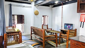 A room with a sofa, a television, a fire blanket, and a woven chair. - The Hub Train House Amazing Gents code (Zanzibar)