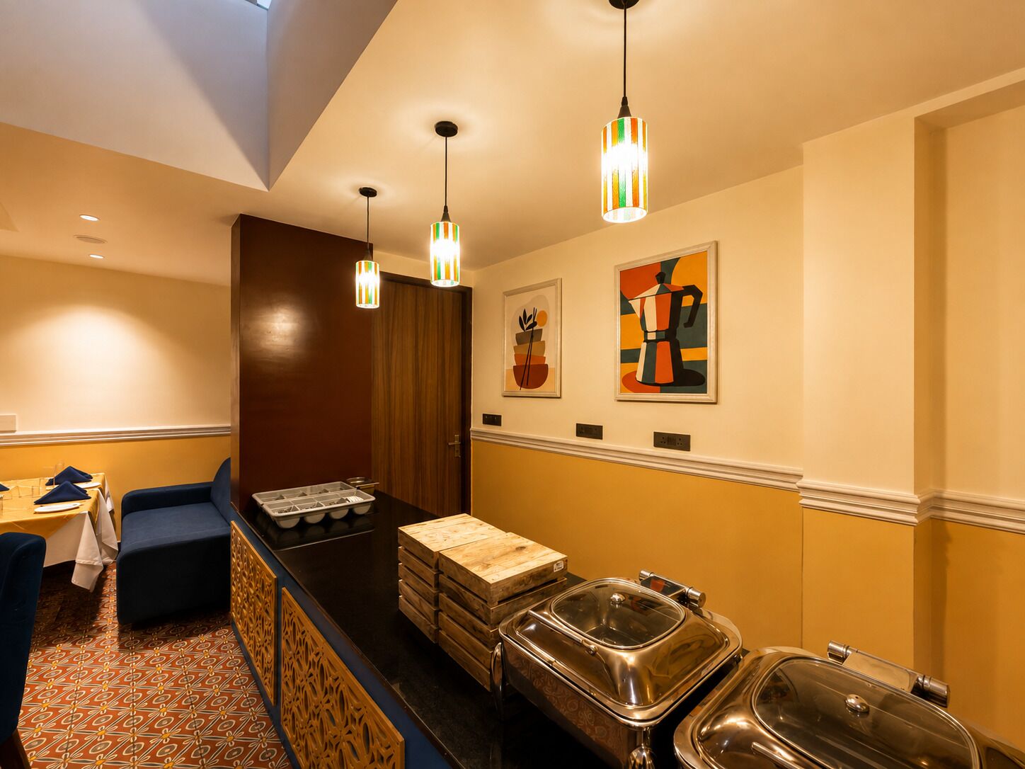 Habitación de hotel con zona de comedor, bufé con recipientes de comida y obras de arte en las paredes.