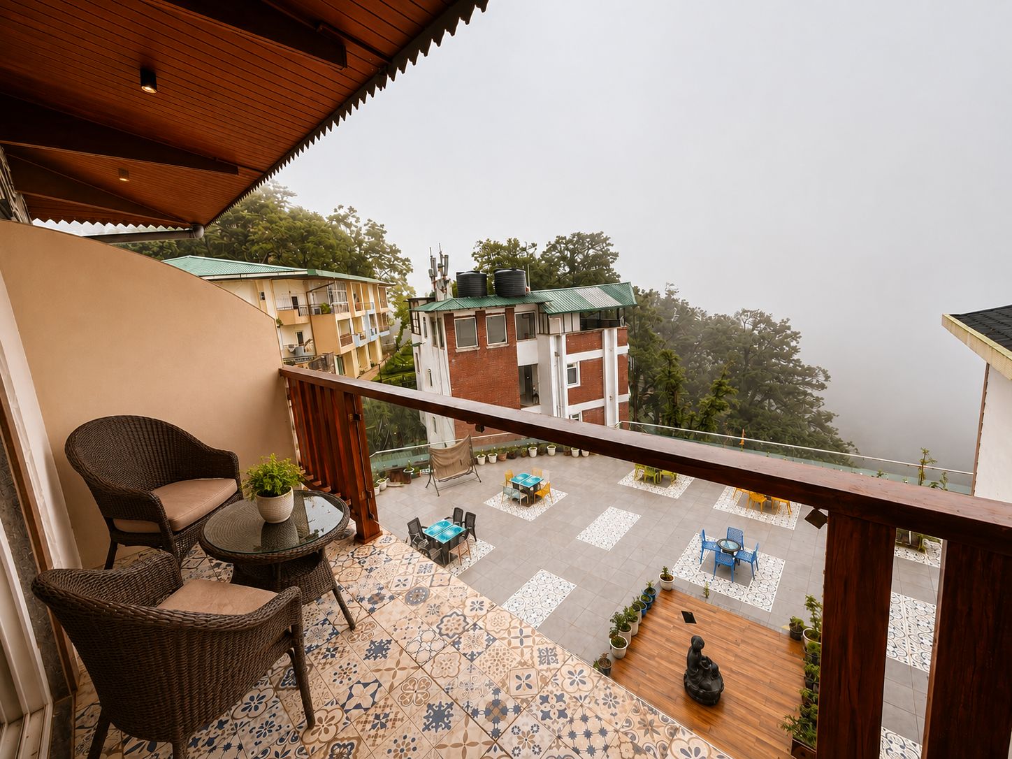 A balcony with wicker furniture, a potted plant, and a view of buildings and trees.