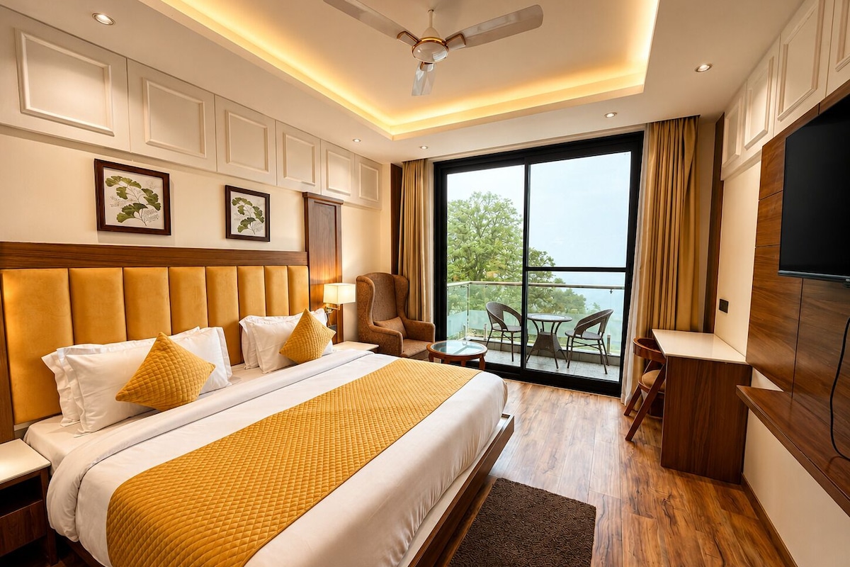 A hotel room with a large bed, a desk, a chair, a TV, and a balcony with a view.