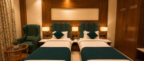 A hotel room with two beds, a green armchair, a small table, and a wardrobe.
