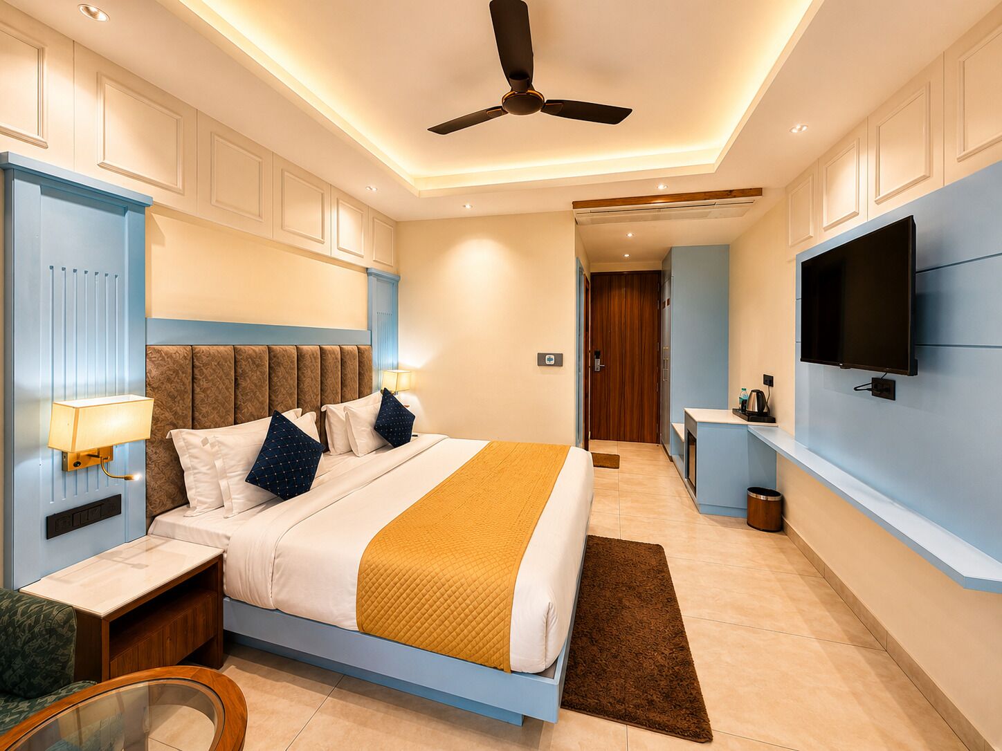 A modern hotel room with a large bed, a ceiling fan, a TV, and a small kitchenette.