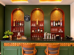 A bar area with a green wall, three arched niches displaying liquor bottles, and two wooden bar stools. - SSH Ardmore Hills (Mussoorie)