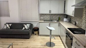 A compact kitchen with a sofa, a bar stool, and a modern stove. - cosy 1bed perfect for family and contractors (Woolwich, London)