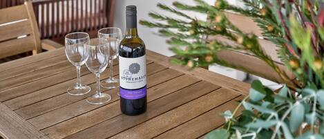 Una mesa de madera con una botella de vino Stonemason Currency Cuvée, cuatro copas de vino vacías y una planta en maceta.