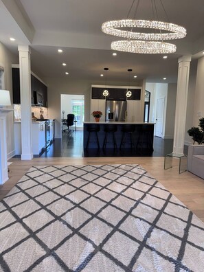 A modern kitchen with a central island, a dining area with a chandelier, and a patterned rug. - Cozy Lakefront House Retreat For Families&Friends (Georgina)
