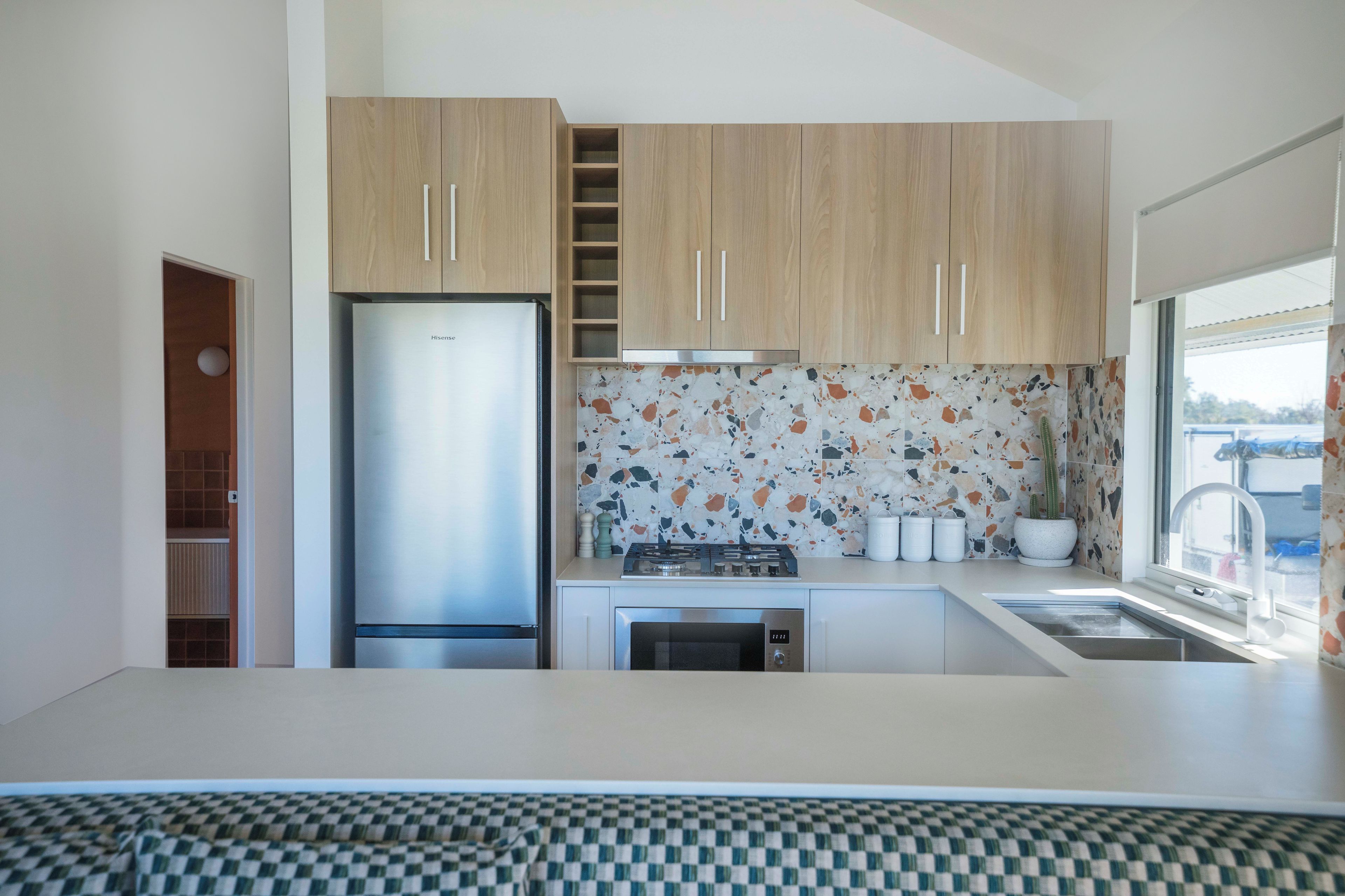 A modern kitchen with wooden cabinets, a stainless steel refrigerator, a gas stove, and a window with a view.