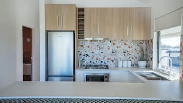 A modern kitchen with wooden cabinets, a stainless steel refrigerator, a gas stove, and a window with a view.