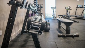 Et fitnessrum med træningsudstyr, herunder håndvægte, kettlebells og en bænk.