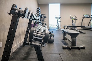 Un gimnasio con equipo de ejercicio, incluyendo mancuernas, kettelbells y una banca.