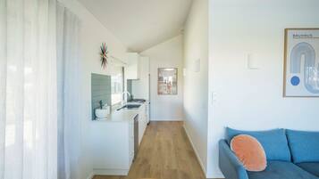A modern living room with a sofa and a coffee table, a kitchen with a sink and cabinets, and a hallway leading to another room.