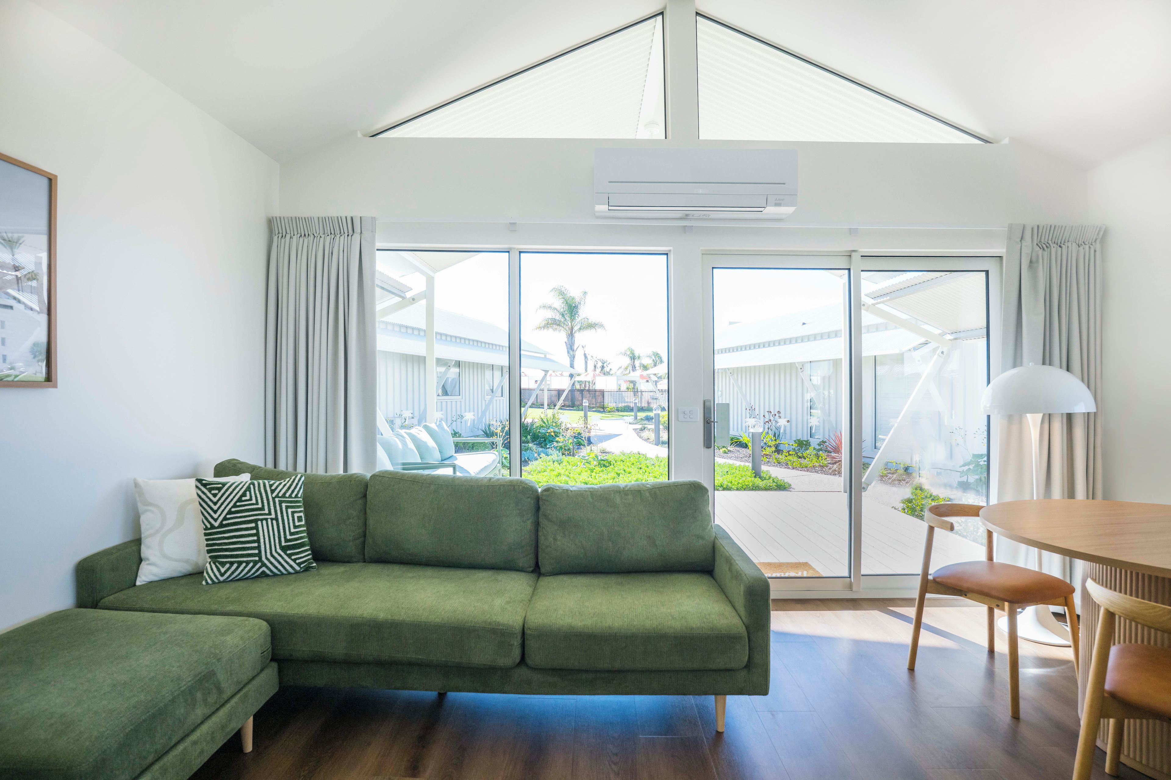A modern living room with a sectional sofa, a dining table with chairs, and a large sliding glass door leading to an outdoor area.