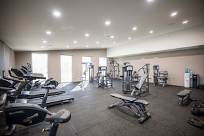 Un gimnasio con varios equipos de ejercicio, incluyendo cintas de correr, máquinas de pesas y pesas sueltas.