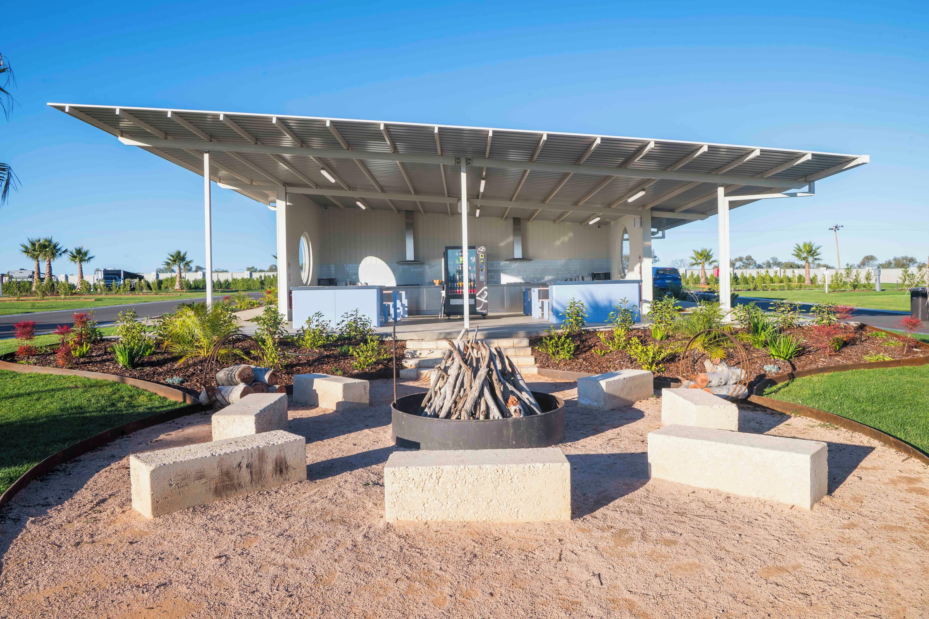 A covered outdoor area with a fire pit, seating, and a view of a modern building in the background.