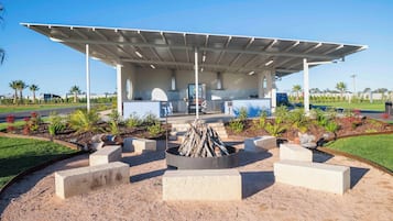 A covered outdoor area with a fire pit, seating, and a view of a modern building in the background.