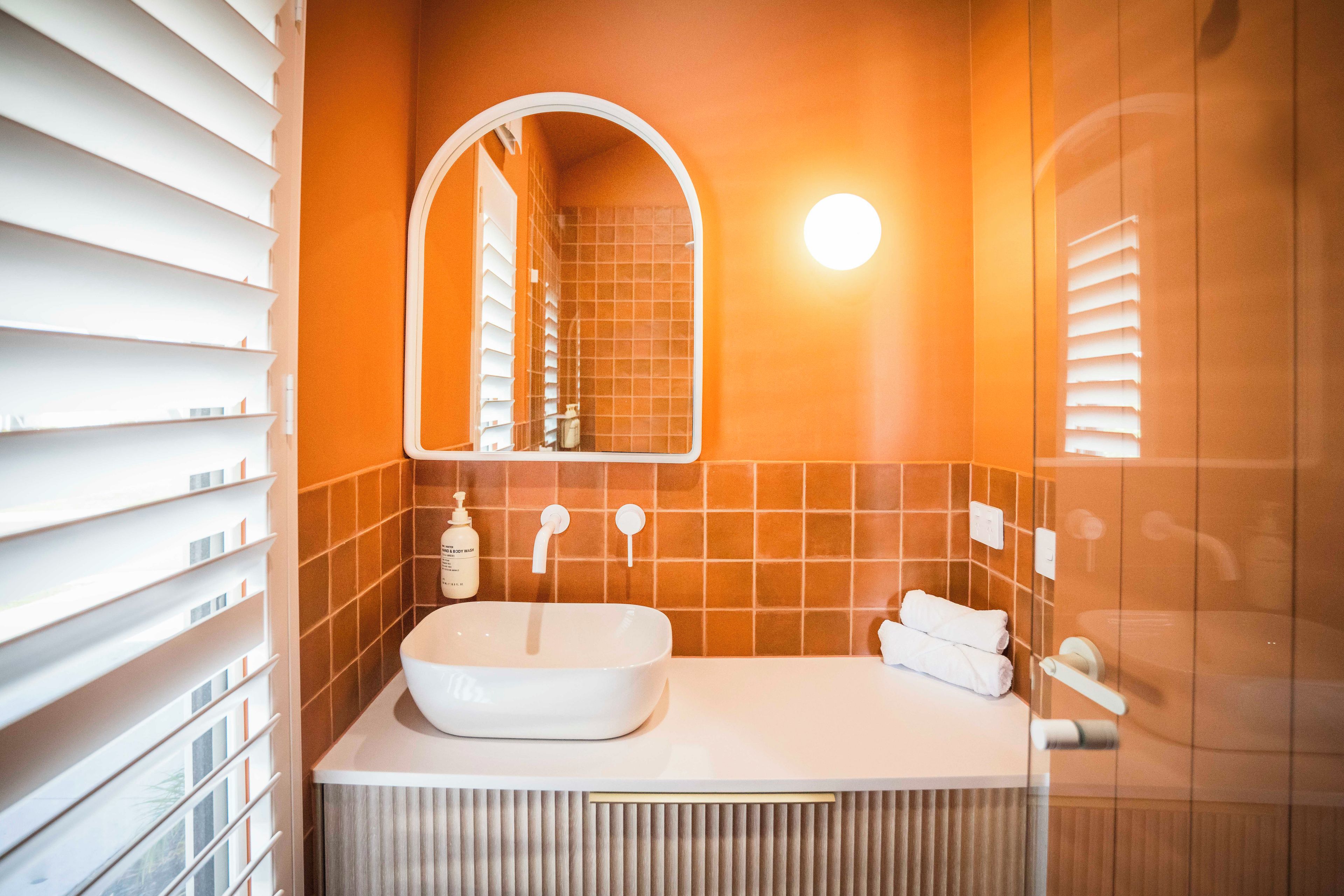 Een badkamer met een wit wastafelmeubel, een spiegel en oranje tegels.
