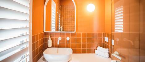 Een badkamer met een wit wastafelmeubel, een spiegel en oranje tegels.
