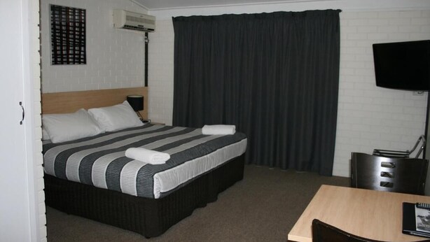 Ein Hotelzimmer mit Bett, Schreibtisch, Stuhl, Fernseher und einer Wandklimaanlage.