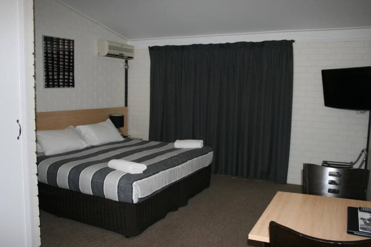 Habitación de hotel con cama, escritorio, silla, televisor y aire acondicionado de pared.