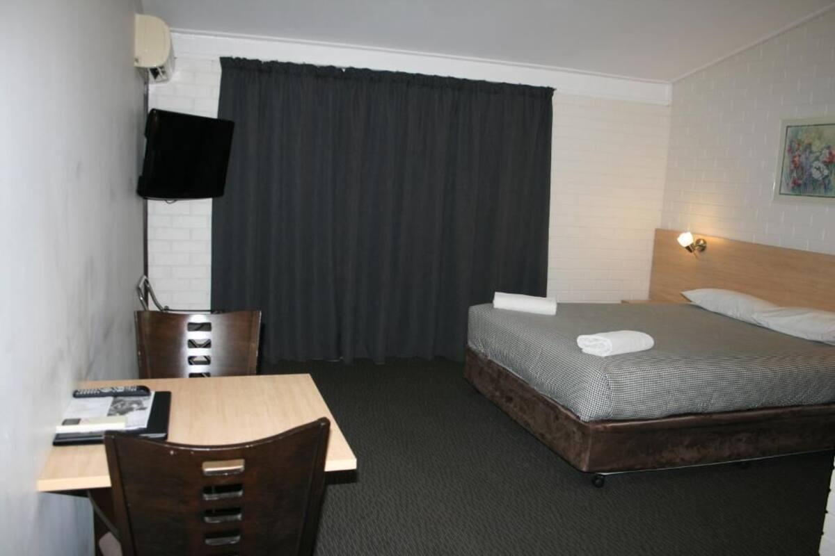 Habitación de hotel con cama, escritorio, silla, televisor montado en la pared y cortina.