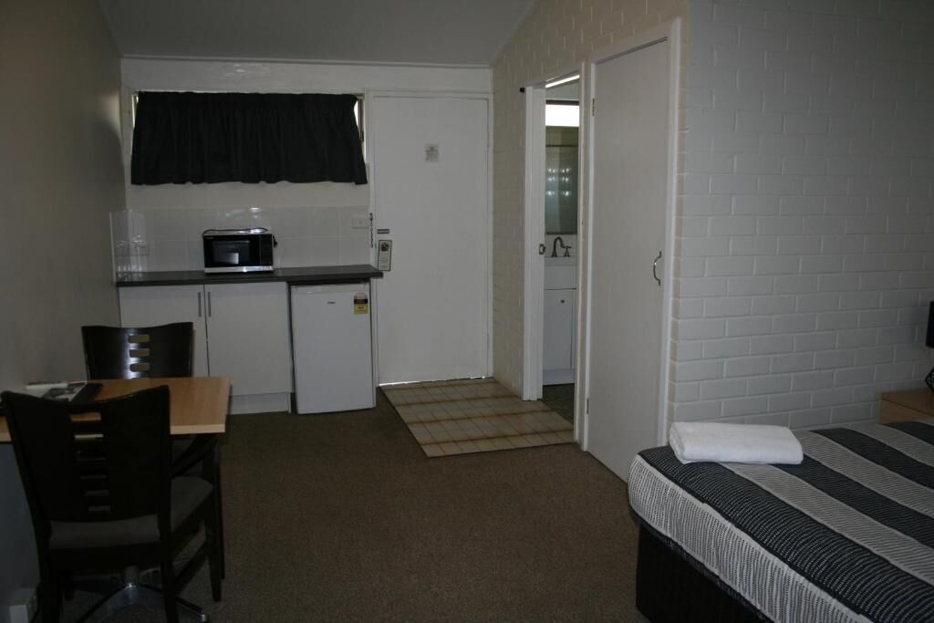 A compact room with a bed, a small kitchenette, and a door leading to a bathroom.