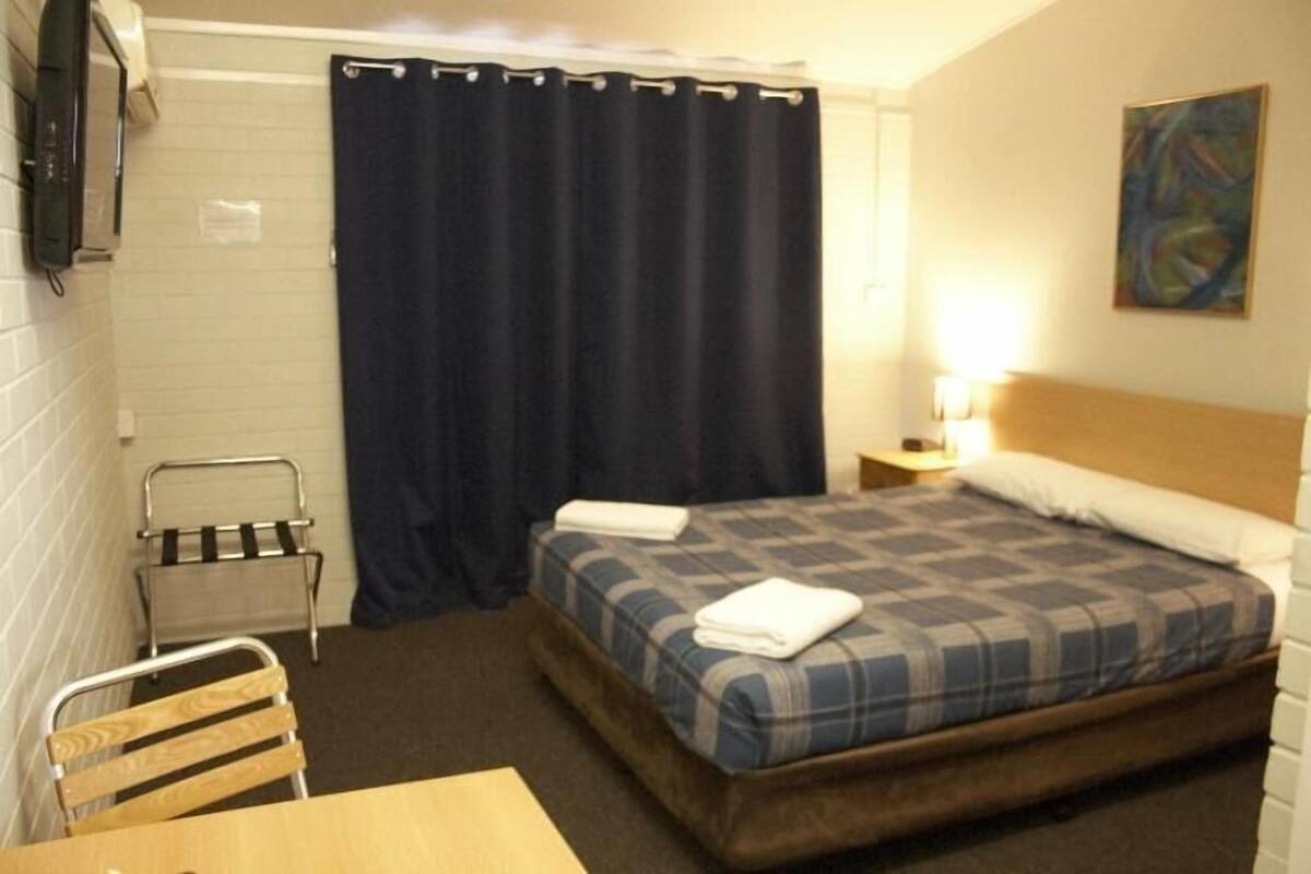 Una habitación pequeña y ordenada con una cama, una silla, una mesa y una cortina.
