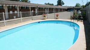 Ein Schwimmbecken mit weißem Zaun, Blumentöpfen und einem Gebäude mit einem Ziegeldach im Hintergrund.