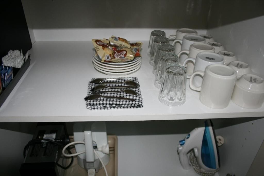 A kitchen counter with a stack of plates, a bowl of snacks, a pair of glasses, and several mugs.