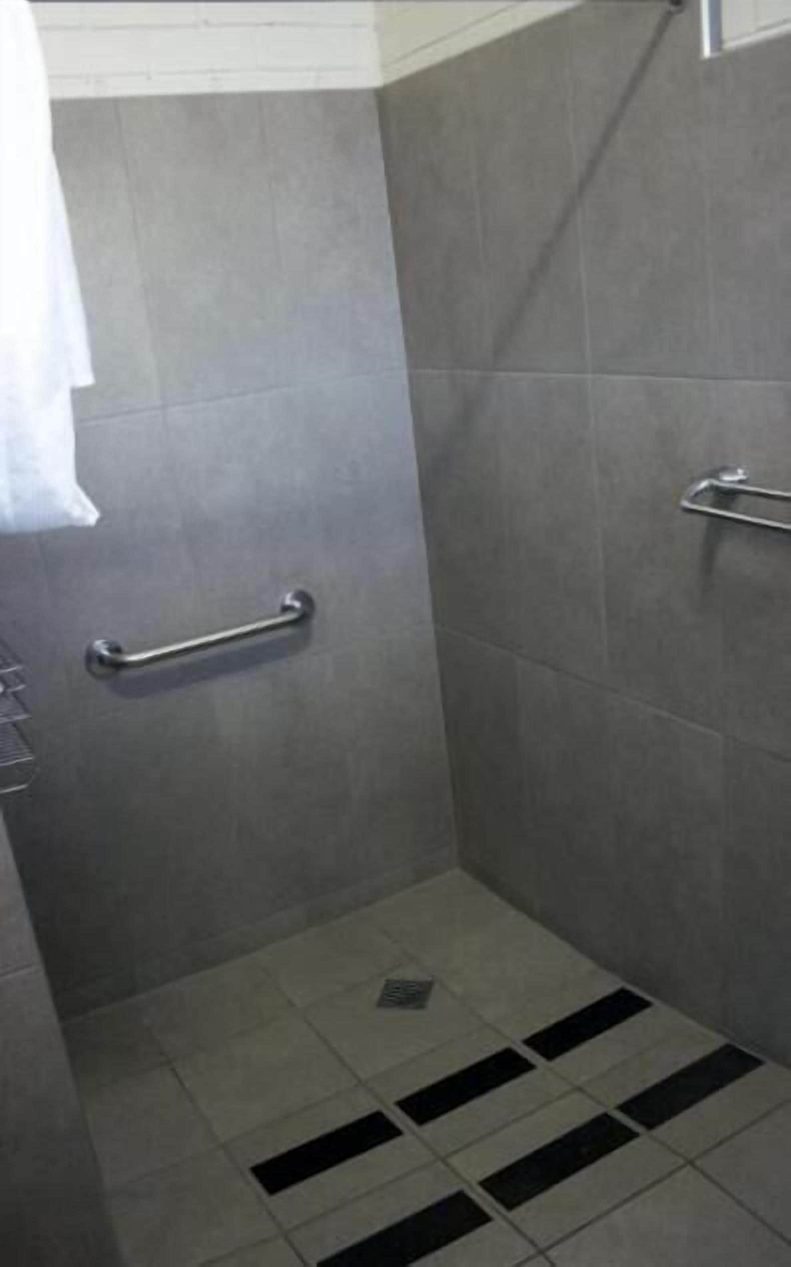 A small, enclosed shower area with a grab bar, tiled walls, and a drain.