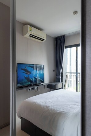 Een moderne hotelkamer met een bed, een wandtelevisie, een airconditioner, een raam met gordijnen en een balkon.