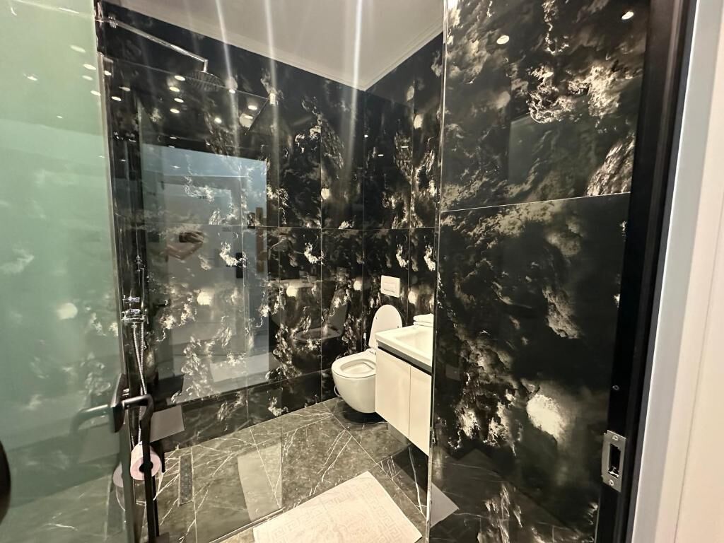 A bathroom with a glass shower enclosure, a toilet, and a sink.