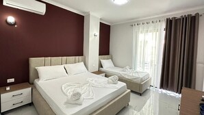 A hotel room with two beds, a desk, a chair, an air conditioning unit, and a window with curtains. - Liel Holiday (Vlore)