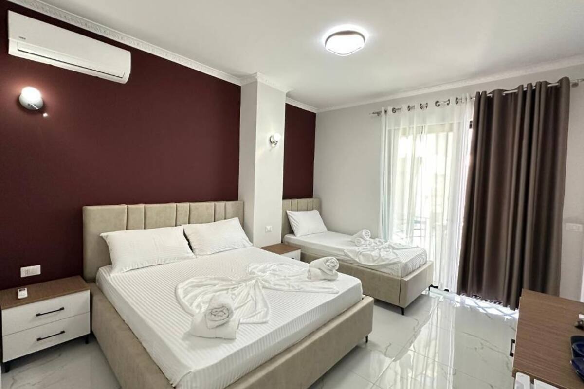 A hotel room with two beds, a desk, a chair, an air conditioning unit, and a window with curtains.