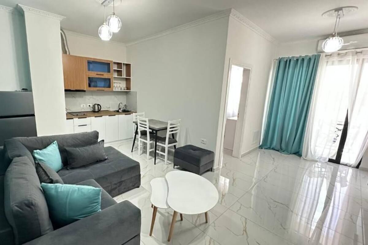 A modern living room with a sofa, a dining table, and a kitchen area with cabinets and a refrigerator.