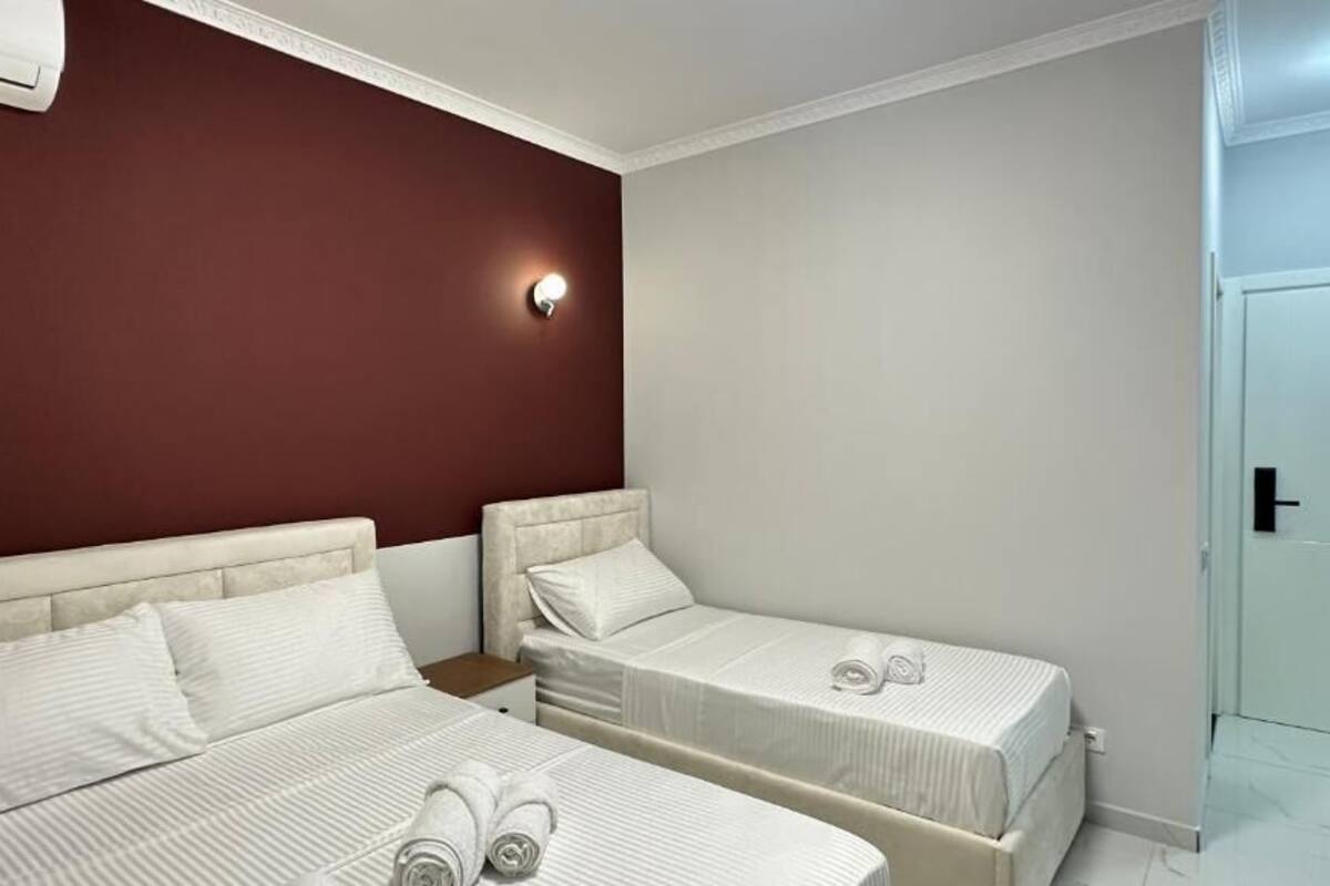A hotel room with two beds, a nightstand, and a wall-mounted light.
