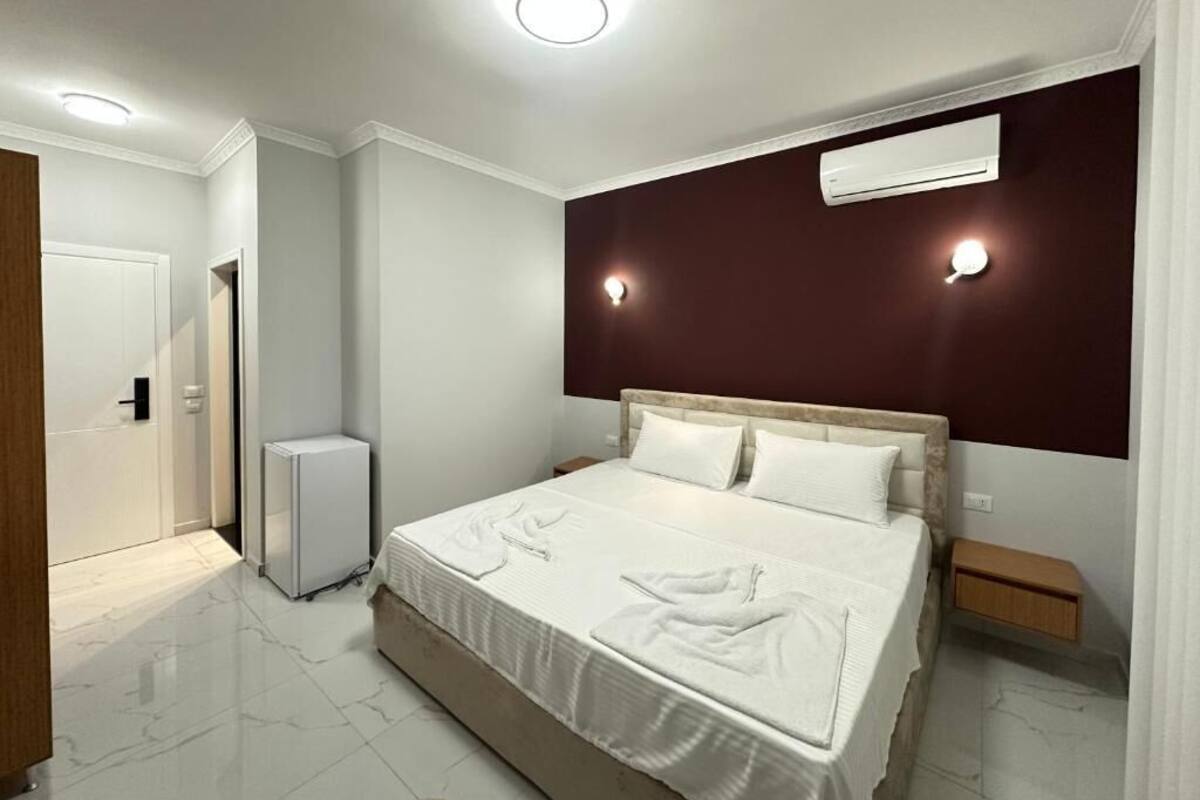 A modern bedroom with a large bed, a bedside table, an air conditioning unit, and a small bedside cabinet.