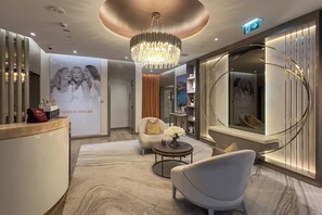 A modern hotel lobby with a reception desk, a chandelier, a round seating area, and a spiral staircase. - Chic 2BR in Paramount Midtown  (Dubai)