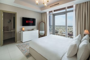 A hotel room with a large bed, a television displaying 'NETFLIX,' a balcony with a view, and a white dresser. - Chic 2BR in Paramount Midtown  (Dubai)