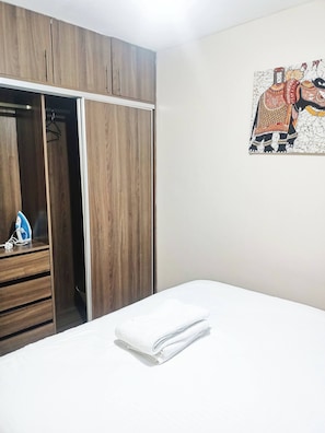 Ein Schlafzimmer mit einem Holfischschrank, einem Bett mit weißer Bettwäsche und einem an der Wand hängenden Kunstwerk.