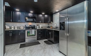 A kitchen with dark cabinets, stainless steel appliances, a microwave, oven, and refrigerator.