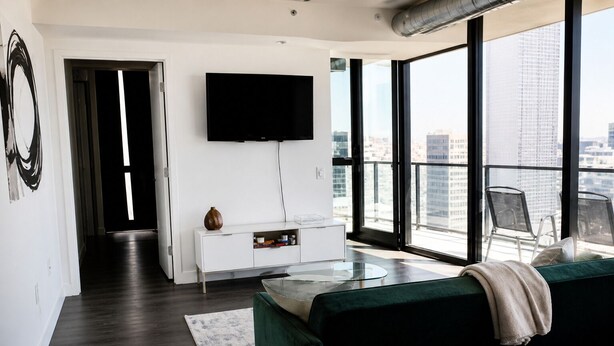 Una sala de estar moderna con un ventanal grande, un televisor de pantalla plana, un sofá verde y un mueble bajo blanco.
