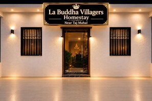 Exterior de La Buddha Villagers Homestay, con una placa, entrada y dos luces fijadas a la pared.